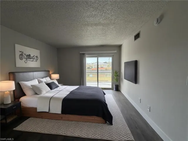 Bedroom with a textured ceiling, access to exterior, and dark wood-style flooring