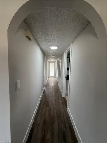 Hall with arched walkways, dark wood-style flooring, and a textured ceiling