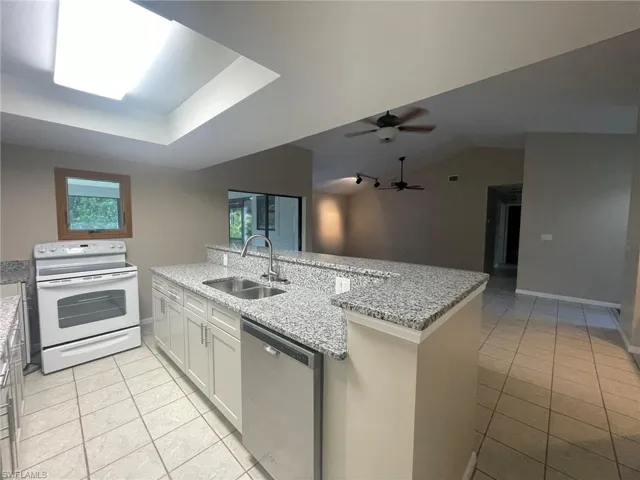 Kitchen featuring white cabinetry, sink, light stone countertops, stainless steel dishwasher, and white electric range