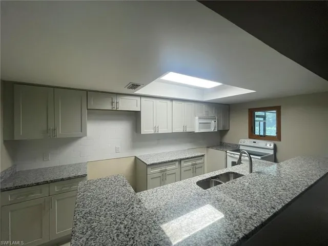 Kitchen featuring tasteful backsplash, light stone counters, white appliances, gray cabinets, and kitchen peninsula