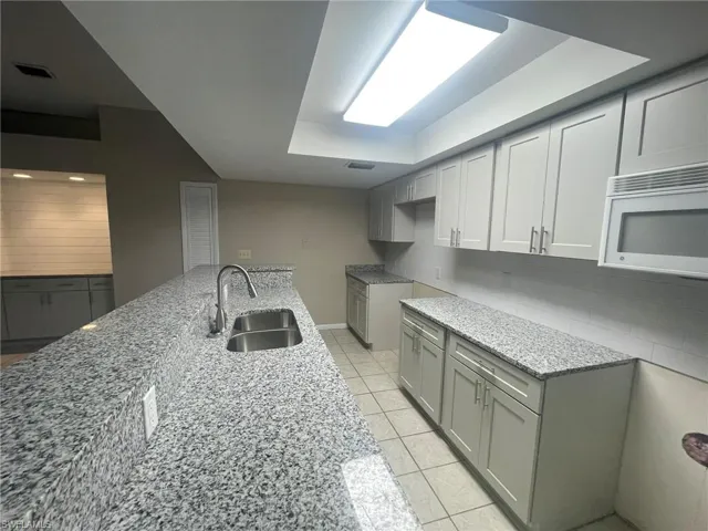 Kitchen featuring light tile patterned floors, sink, decorative backsplash, and light stone counters