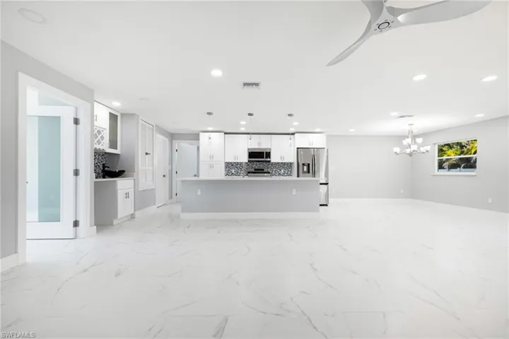 Unfurnished living room with light marble finish flooring, recessed lighting, ceiling fan, and a chandelier