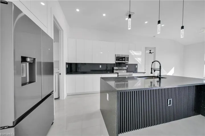 Kitchen featuring stainless steel appliances, modern cabinets, white cabinetry, decorative light fixtures, and dark stone counters