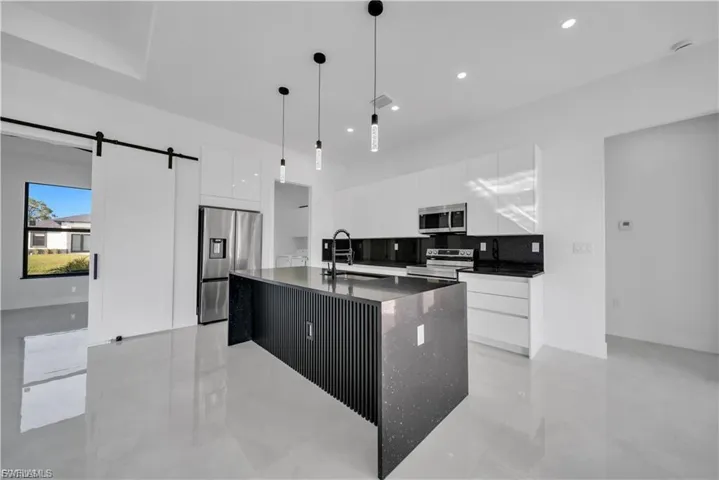 Kitchen featuring modern cabinets, appliances with stainless steel finishes, dark stone counters, white cabinetry, and a barn door