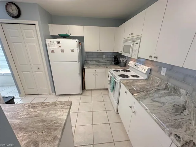 Kitchen featuring white appliances, white cabinetry, light tile patterned floors, and light stone countertops