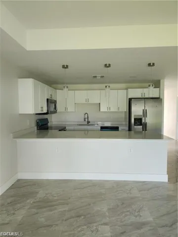 Kitchen featuring white cabinets, a peninsula, black appliances, light countertops, and decorative light fixtures