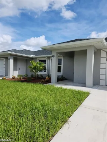 Entrance to property with stucco siding, a garage, a lawn, and driveway
