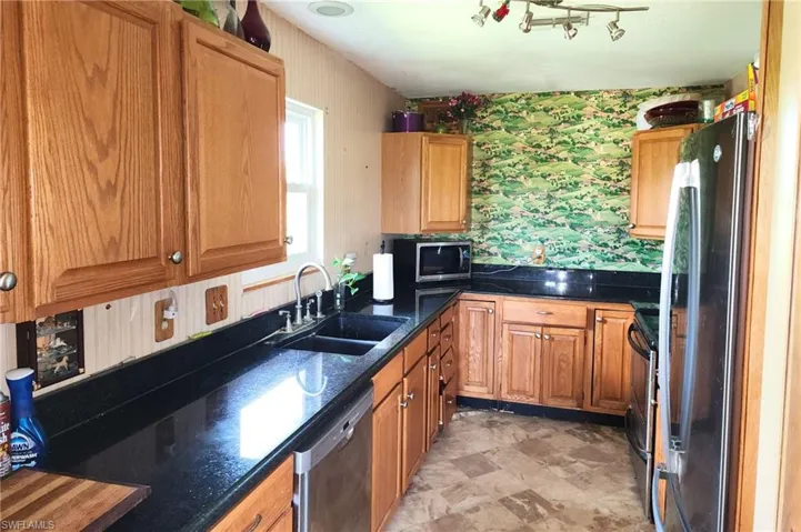 Kitchen featuring wallpapered walls, stainless steel appliances, brown cabinets, dark stone counters, and stone finish flooring