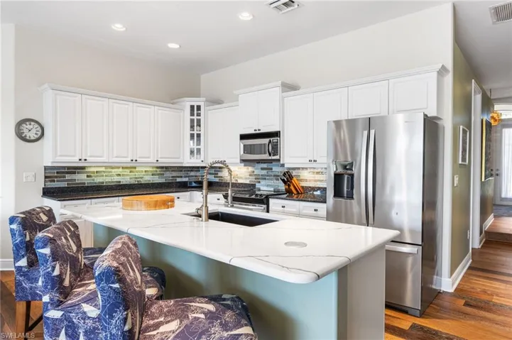 This kitchen pulls out all the stops—custom white cabinetry, a subway tile backsplash with underlighting, sleek stainless steel appliances, quartz countertops with not one but two pop-up charging stations (because even your phone deserves luxury), all glowing under perfectly placed recessed lighting.