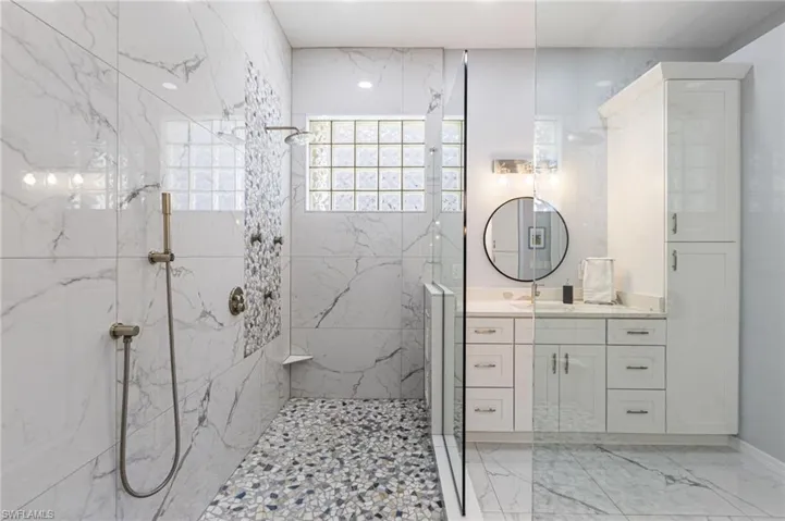 Floor-to-ceiling crafted porcelain tile, accented with a stunning listello, creates a refined spa-like atmosphere, while natural light fills the space, enhancing its calm and airy feel.