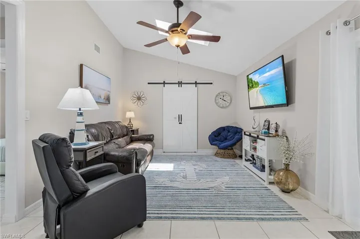 Living room with ceiling fan, light tile floors, and lofted ceiling