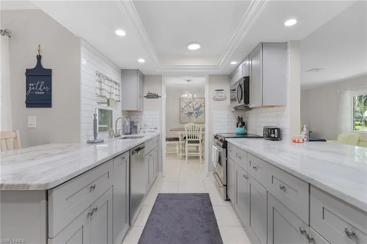Kitchen with a tray ceiling, backsplash, light stone counters, and stainless steel appliances