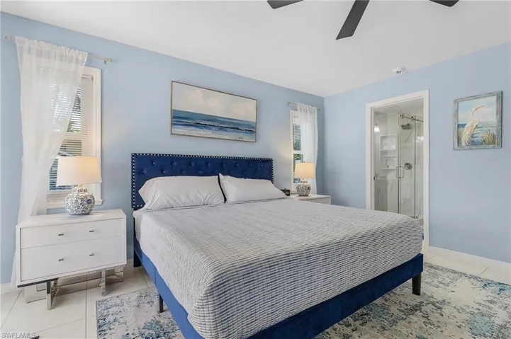 Bedroom featuring ceiling fan, ensuite bathroom, and light tile floors