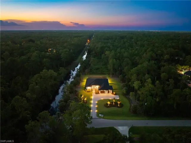 Spacious property featuring a prominent single-story residence, a long paved driveway, manicured lawns with mature trees, and a bordering waterway