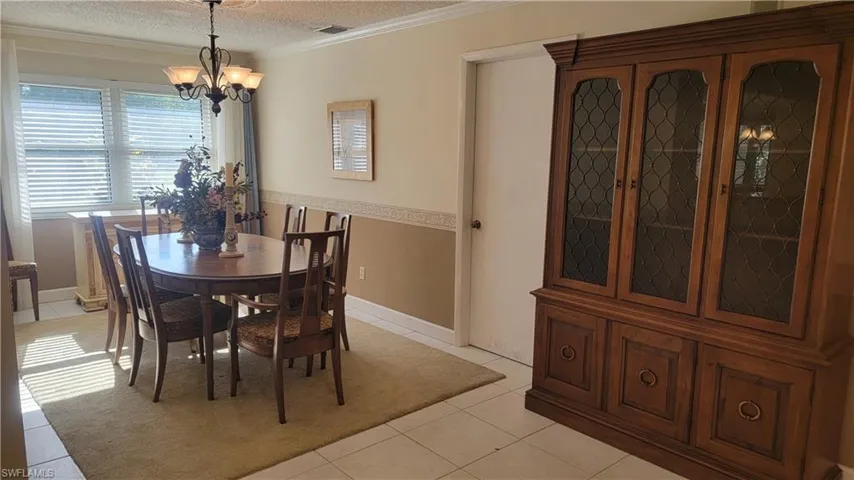 Tiled dining room featuring ornamental molding, a textured ceiling, and an inviting chandelier