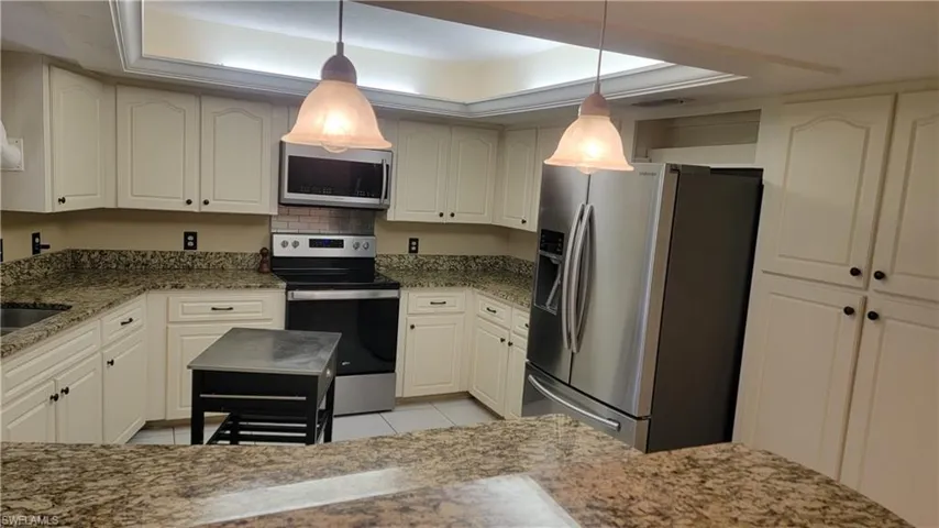 Kitchen with stainless steel appliances, a raised ceiling, and pendant lighting