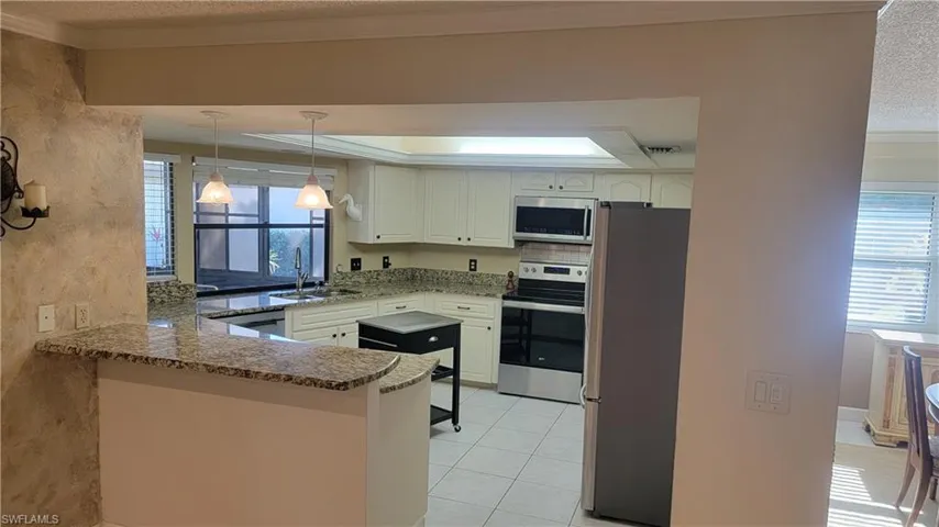 Kitchen with appliances with stainless steel finishes, pendant lighting, dark stone counters, ornamental molding, and kitchen peninsula