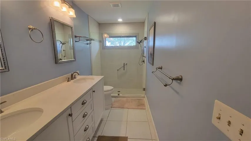 Bathroom with a shower with door, vanity, tile patterned flooring, and toilet