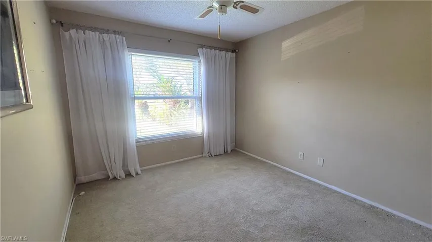 Empty room featuring ceiling fan, light colored carpet, and a textured ceiling