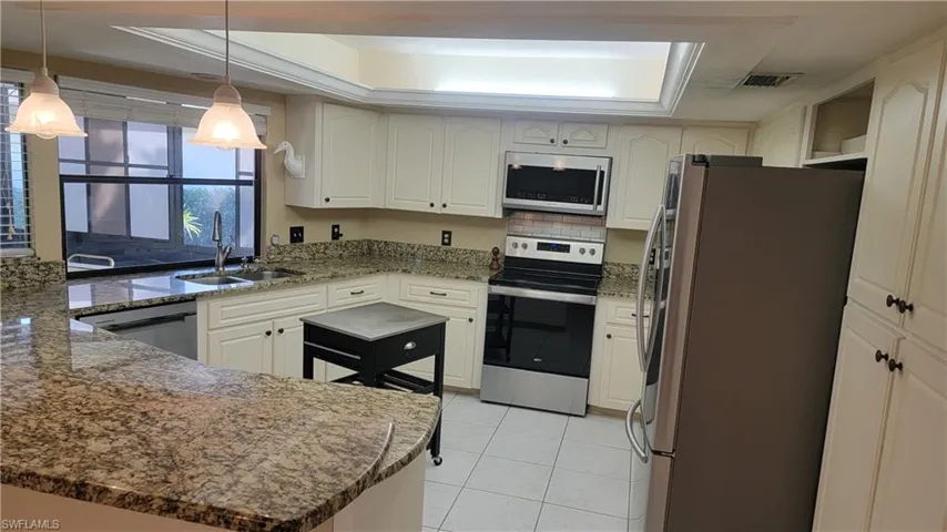 Kitchen with sink, decorative light fixtures, light tile patterned floors, dark stone counters, and stainless steel appliances