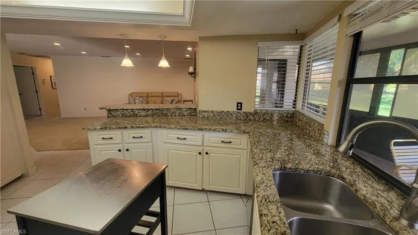 Kitchen with sink, white cabinetry, a kitchen island, decorative light fixtures, and light tile patterned flooring