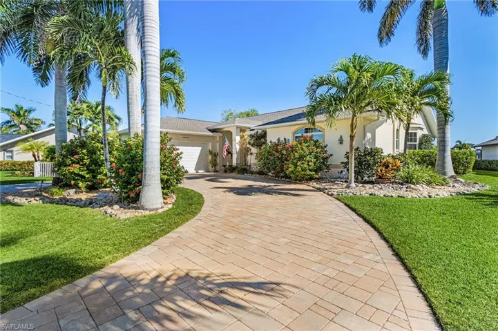 Ranch-style home with a front yard, stucco siding, an attached garage, and decorative driveway