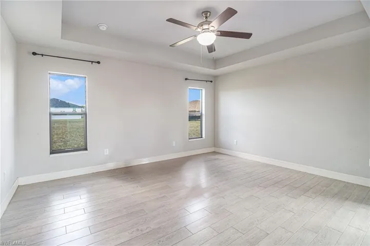 Empty room with a tray ceiling, tile wood-type flooring, and ceiling fan