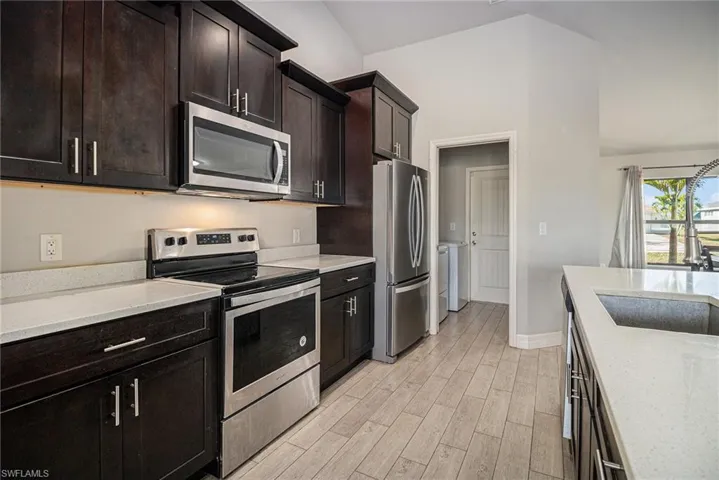 Kitchen with appliances with stainless steel finishes, light stone countertops, dark brown cabinets, wood tiled floors, and washer and dryer