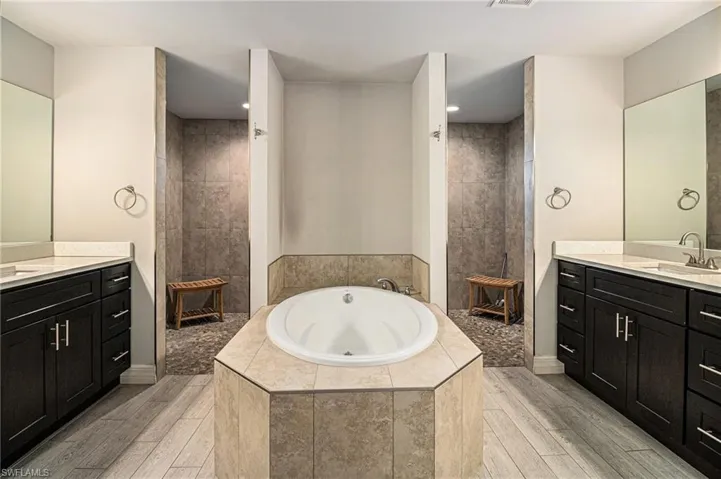 Full bathroom featuring a bath, light wood-type flooring, two vanities, and walk in shower