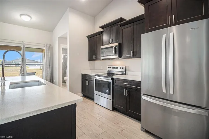 Kitchen with stainless steel appliances, light stone countertops, tile wood-type flooring, and dark brown cabinets