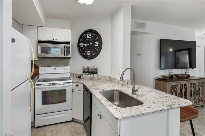 Kitchen featuring a peninsula, light stone countertops, decorative backsplash, and white cabinets