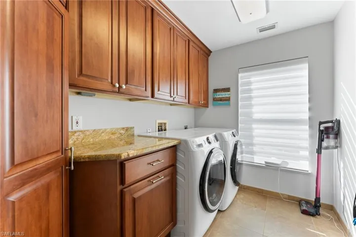 Laundry area with light tile patterned flooring, washer and clothes dryer, and cabinet space