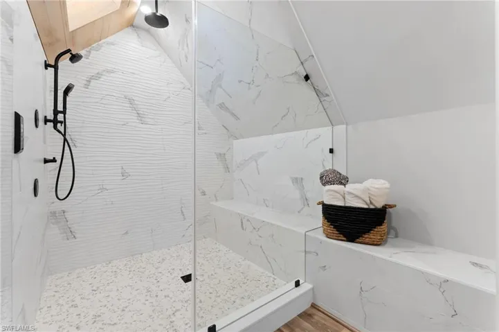 Bathroom with a marble finish shower, lofted ceiling, and wood finished floors