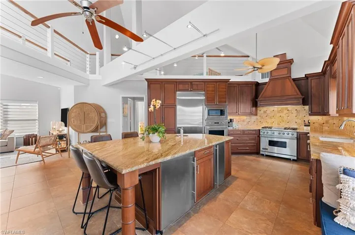 Kitchen featuring a ceiling fan, a high ceiling, light stone countertops, a breakfast bar, and backsplash