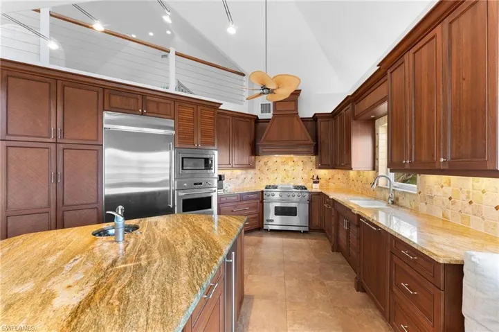 Kitchen with built in appliances, light stone counters, tasteful backsplash, custom exhaust hood, and light tile patterned floors