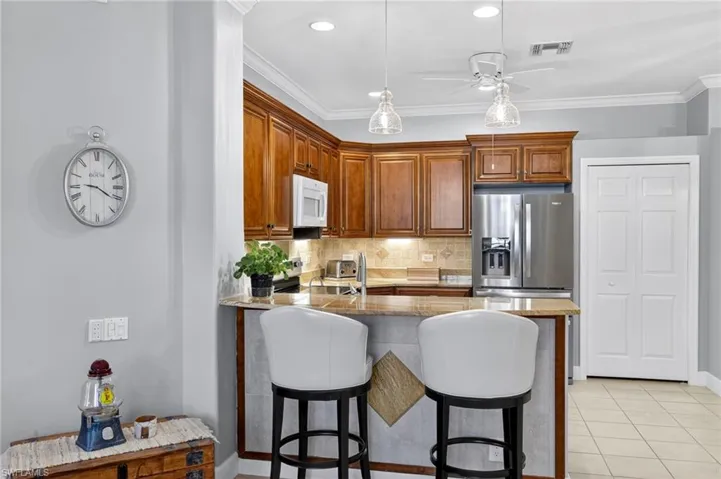 Kitchen with decorative backsplash, a kitchen bar, light stone counters, brown cabinetry, and island.