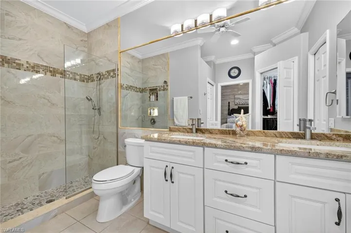 Bathroom featuring a shower stall, a spacious closet, ornamental molding, light tile patterned flooring, and a ceiling fan