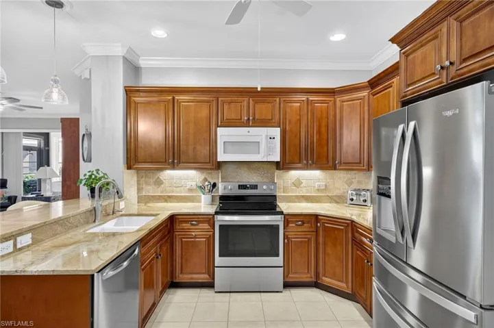 Kitchen featuring ceiling fan, stainless steel appliances, light stone countertops, ornamental molding, and tasteful backsplash