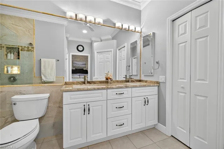 Ensuite bathroom with a closet, tile walls, ornamental molding, and light tile patterned flooring