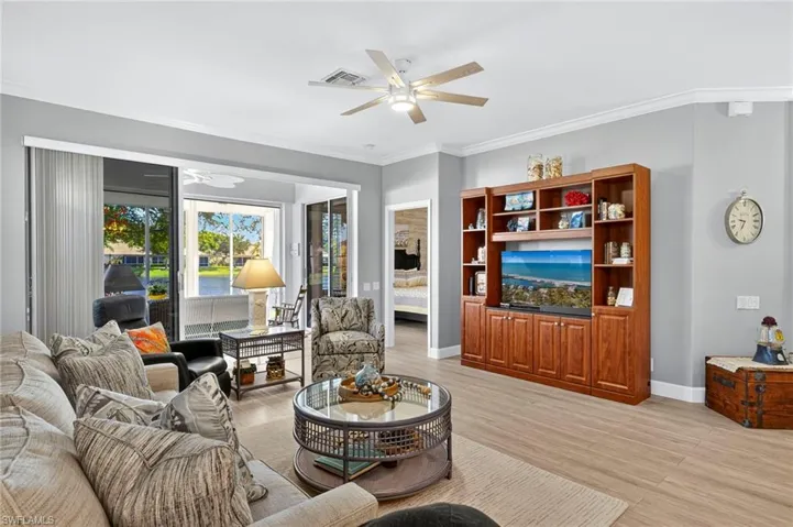 Living room featuring ornamental molding, light wood-style flooring, ceiling fan, and a sunroom