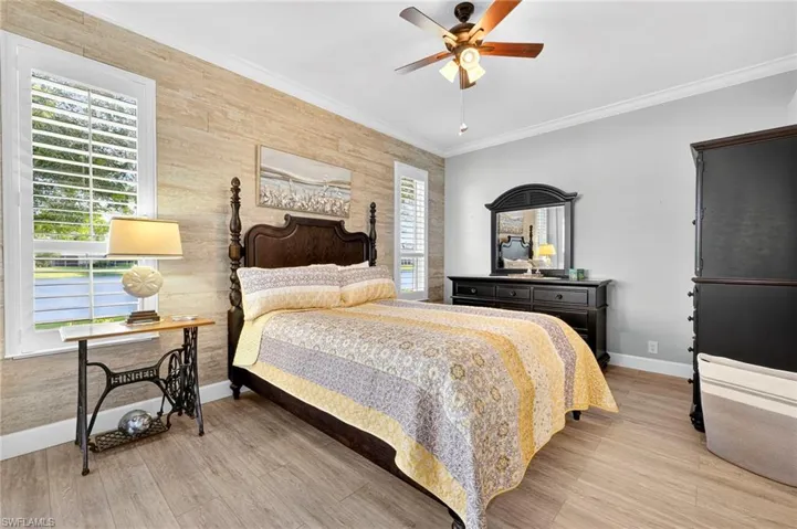 Bedroom with ornamental molding, light wood-type flooring, ceiling fan, and an accent wall