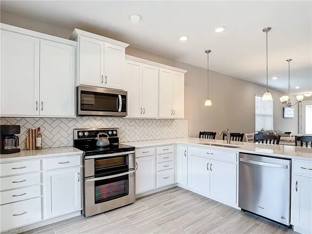 Kitchen featuring appliances with stainless steel finishes, a sink, light countertops, decorative light fixtures, and recessed lighting