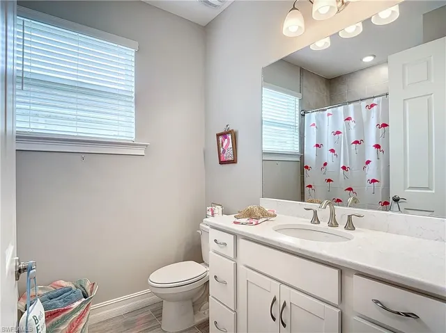 Bathroom with toilet, vanity, a shower with shower curtain, wood finished floors, and baseboards