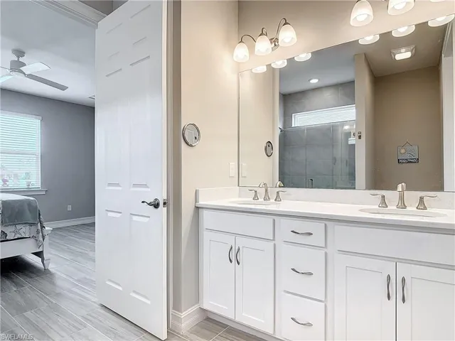 Bathroom with a shower stall, ceiling fan, double vanity, baseboards, and ensuite bathroom