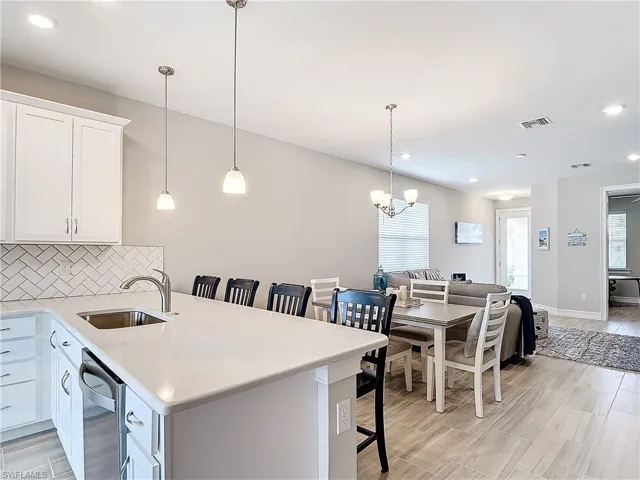 Kitchen featuring a sink, a kitchen bar, tasteful backsplash, white cabinets, and a chandelier