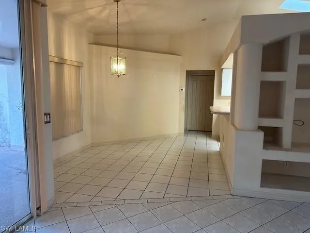 Unfurnished dining area with lofted ceiling, light tile patterned floors, and a chandelier