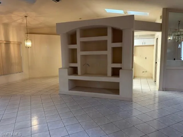 Unfurnished living room with built in shelves, tile patterned flooring, and a chandelier