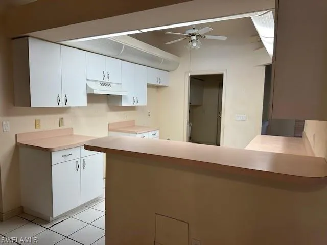 Kitchen with a peninsula, light countertops, ceiling fan, white cabinetry, and light tile patterned floors