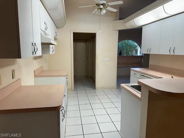 Kitchen with light countertops, a ceiling fan, light tile patterned floors, white cabinets, and a peninsula