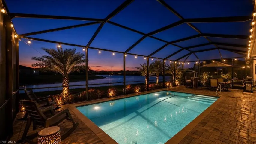 Screened lanai featuring a swimming pool, paver deck, string lighting, mature palm trees, and waterfront exposure